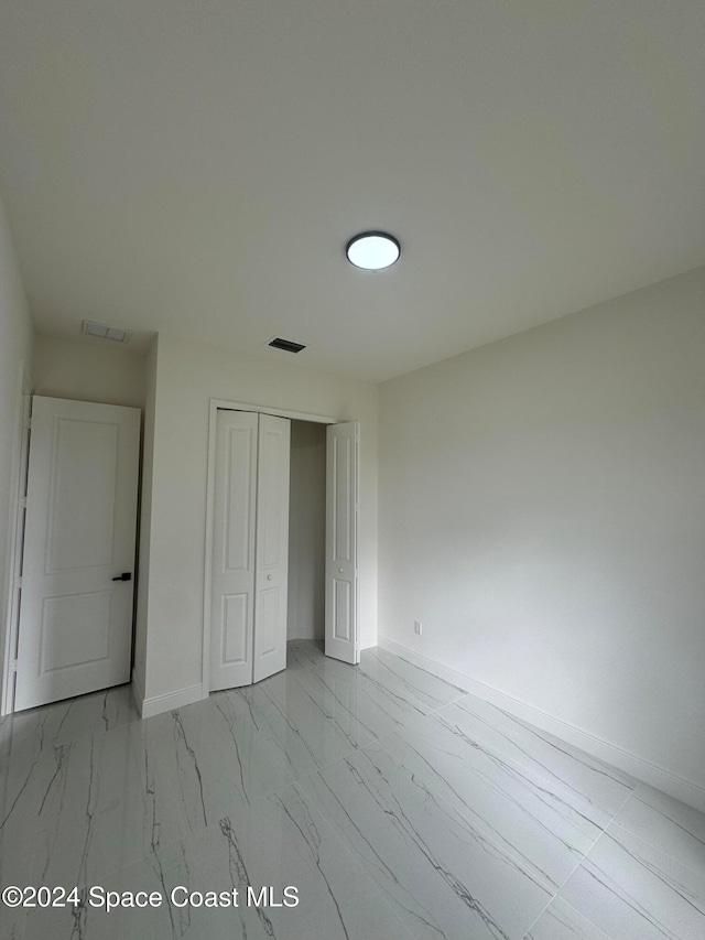 unfurnished bedroom featuring marble finish floor, visible vents, baseboards, and a closet