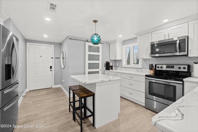 kitchen with light wood-type flooring, stainless steel appliances, a center island, and light stone countertops