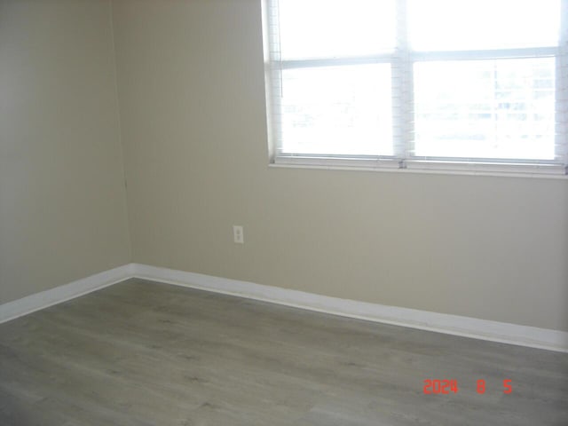 unfurnished room featuring baseboards, wood finished floors, and a healthy amount of sunlight