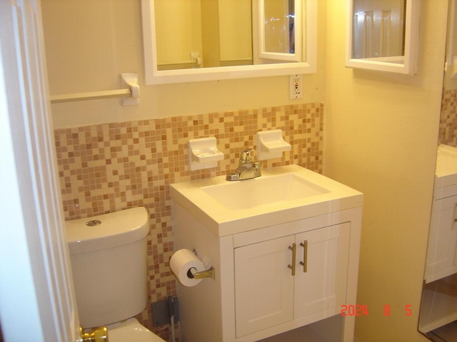 half bath featuring tile walls, a wainscoted wall, vanity, and toilet