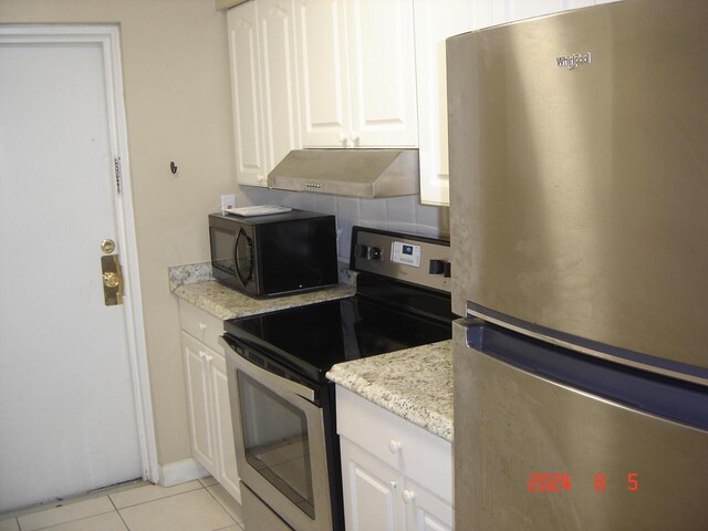 kitchen with light tile patterned flooring, wall chimney range hood, white cabinets, stainless steel appliances, and decorative backsplash