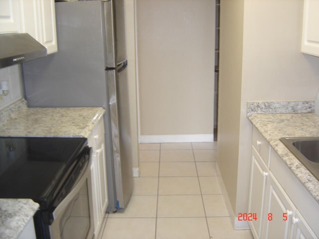 kitchen with black electric range oven, light tile patterned flooring, white cabinets, and wall chimney range hood