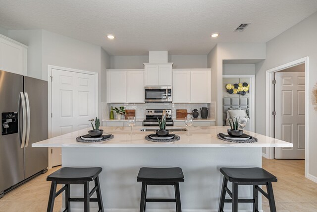 kitchen featuring white cabinets, a kitchen bar, an island with sink, and appliances with stainless steel finishes