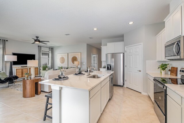 kitchen with sink, white cabinets, decorative backsplash, stainless steel appliances, and a center island with sink