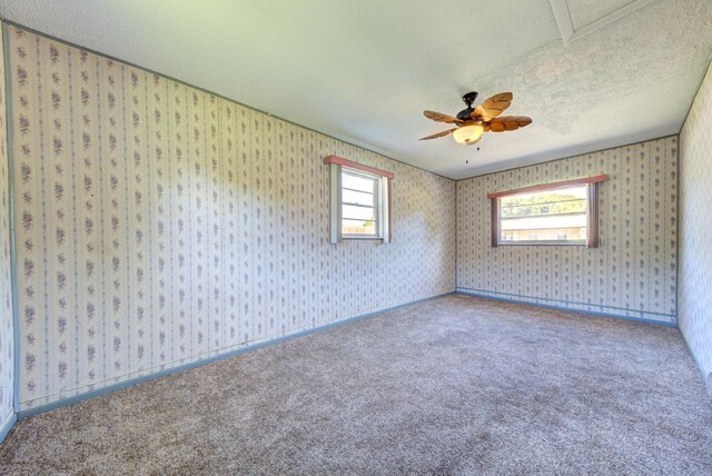 carpeted spare room with wallpapered walls, a ceiling fan, baseboards, and a textured ceiling