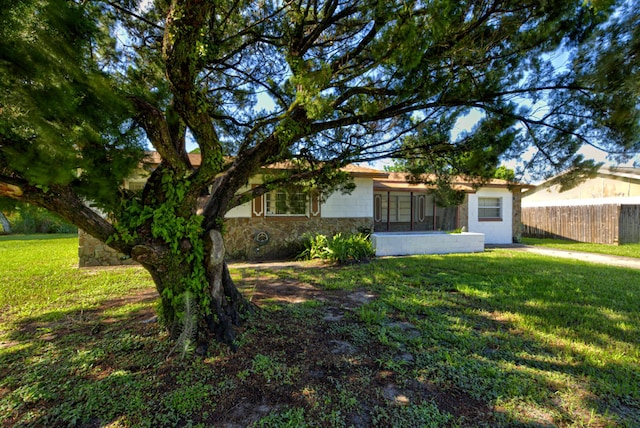 ranch-style home featuring stone siding, a front yard, and fence