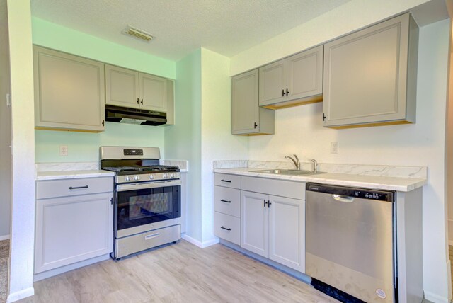 kitchen featuring gas stove, light wood-type flooring, sink, dishwasher, and a textured ceiling