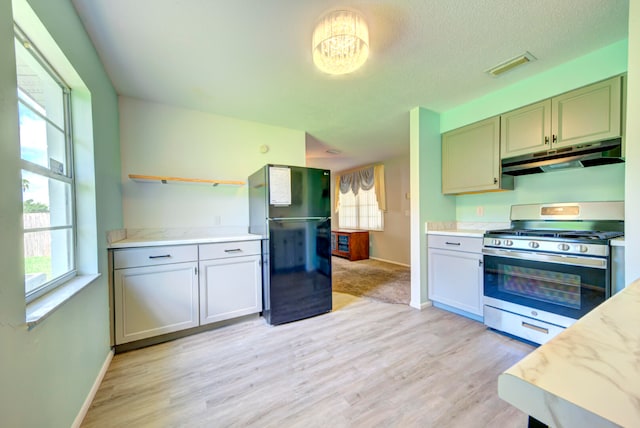 kitchen featuring gas stove, light stone countertops, black refrigerator, and light wood-type flooring