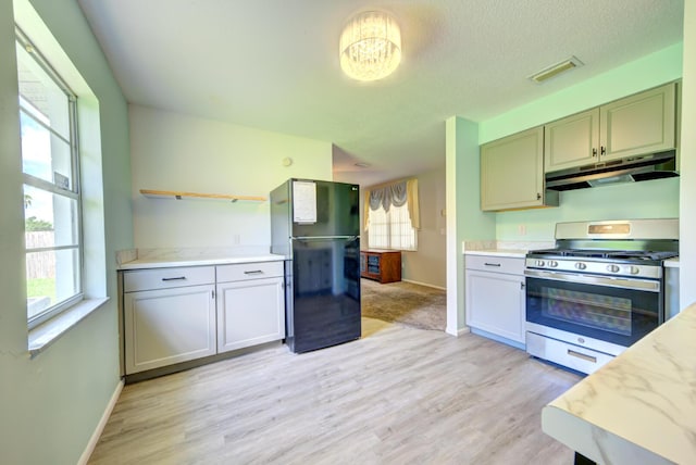 kitchen with under cabinet range hood, visible vents, freestanding refrigerator, open shelves, and stainless steel range with gas stovetop