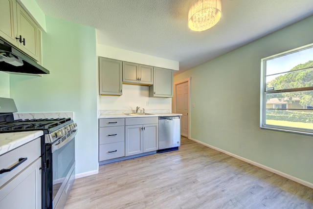 kitchen with light wood-style flooring, stainless steel appliances, a textured ceiling, under cabinet range hood, and a sink