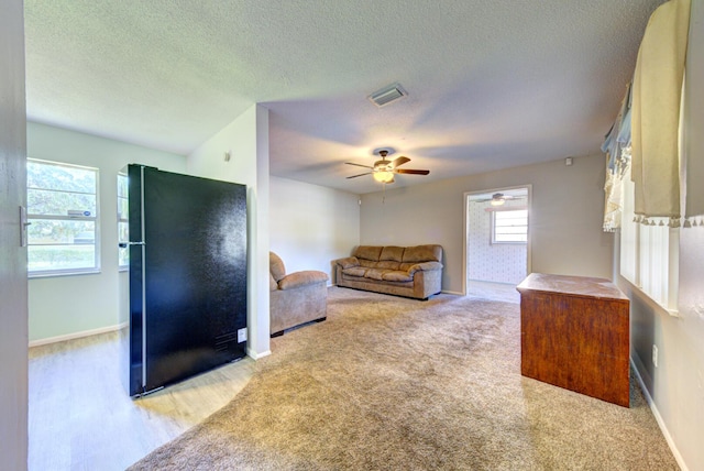 living area featuring a textured ceiling, ceiling fan, light colored carpet, visible vents, and baseboards