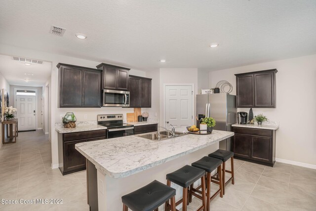 kitchen with stainless steel appliances, sink, dark brown cabinetry, a kitchen breakfast bar, and an island with sink