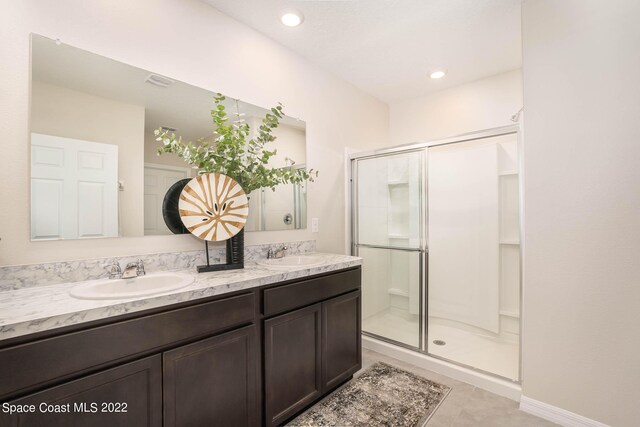 bathroom with tile patterned floors, a shower with door, and dual bowl vanity