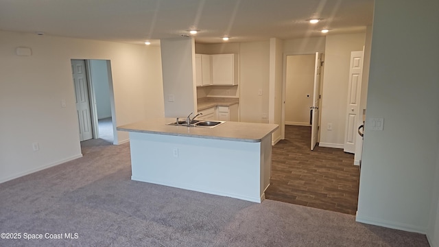 kitchen featuring white cabinets, dark carpet, sink, and an island with sink