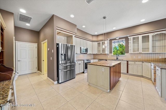 kitchen featuring light tile patterned floors, stainless steel appliances, a center island, light stone counters, and decorative light fixtures