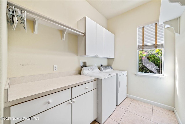 laundry room with light tile patterned floors, a wealth of natural light, washer and clothes dryer, and cabinets