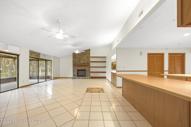 unfurnished living room with ceiling fan, lofted ceiling, a fireplace, a textured ceiling, and light tile patterned flooring