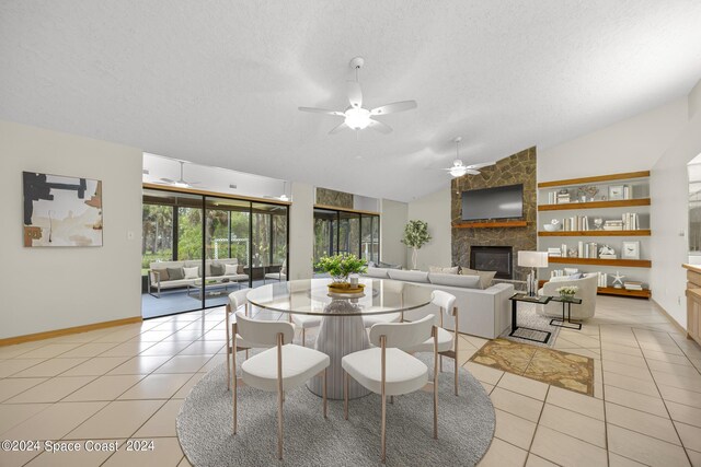 dining area featuring ceiling fan, vaulted ceiling, light tile patterned flooring, and a stone fireplace