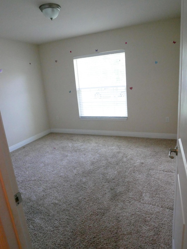 spare room featuring light carpet and baseboards