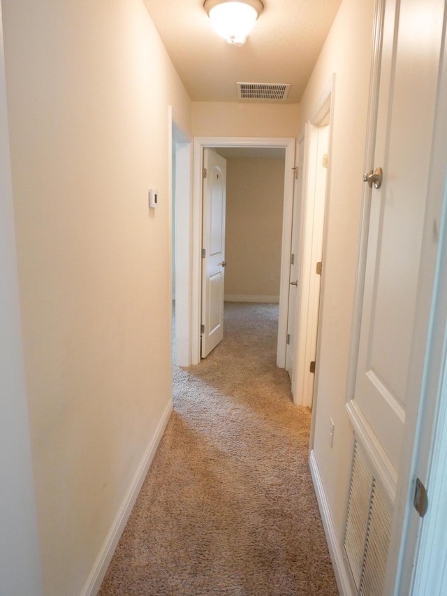 hall featuring baseboards, visible vents, and light colored carpet