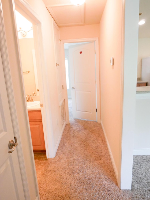 hallway featuring light colored carpet, a sink, and baseboards