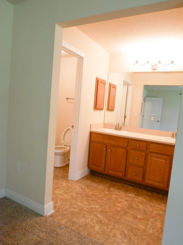 bathroom featuring baseboards, a sink, toilet, and double vanity