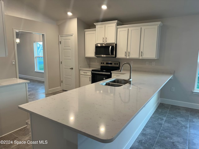 kitchen with kitchen peninsula, appliances with stainless steel finishes, a kitchen breakfast bar, white cabinetry, and sink