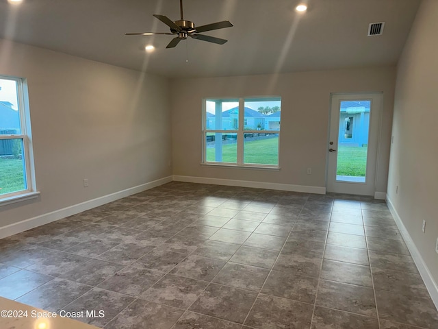 empty room with dark tile patterned flooring, plenty of natural light, and ceiling fan