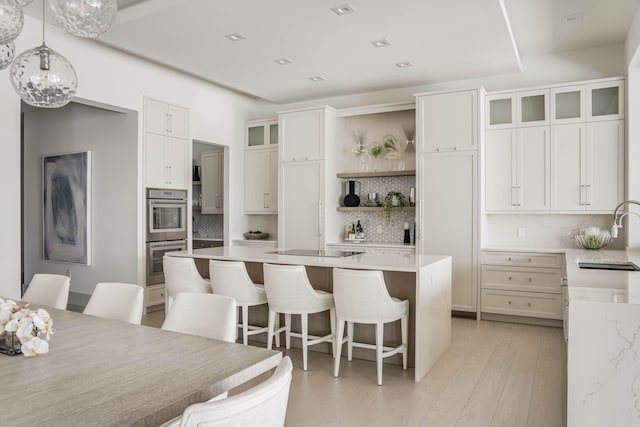 kitchen featuring light hardwood / wood-style flooring, tasteful backsplash, a kitchen island, stainless steel double oven, and pendant lighting