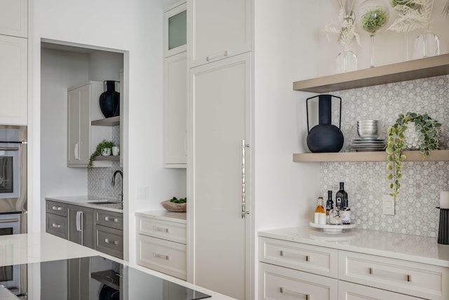 kitchen featuring tasteful backsplash, stainless steel oven, white cabinets, oven, and sink