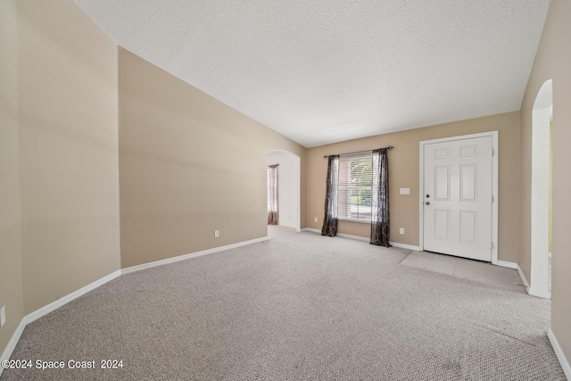 unfurnished room featuring light carpet, a textured ceiling, and lofted ceiling