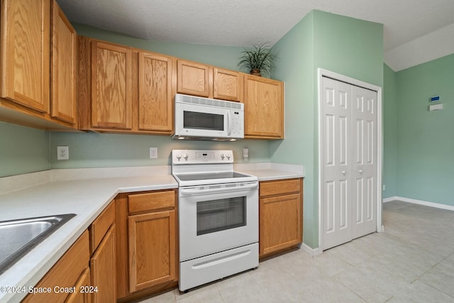 kitchen with a textured ceiling, white appliances, sink, lofted ceiling, and light tile patterned flooring