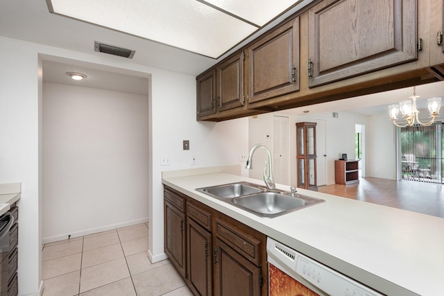 kitchen with light tile patterned floors, dark brown cabinets, white dishwasher, sink, and a chandelier