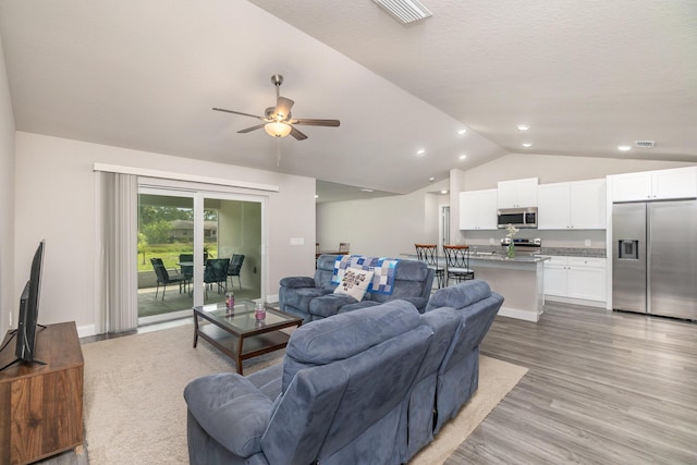 living room featuring ceiling fan, lofted ceiling, and light hardwood / wood-style flooring