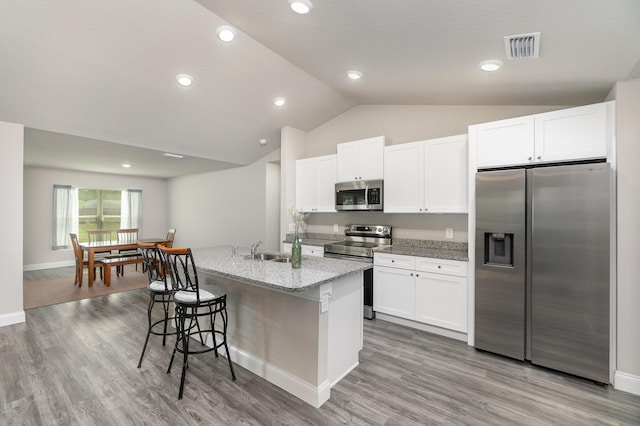 kitchen with a kitchen island with sink, light stone counters, stainless steel appliances, and white cabinets