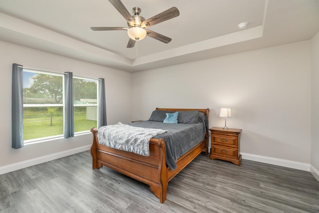 bedroom with dark hardwood / wood-style flooring, a tray ceiling, and ceiling fan