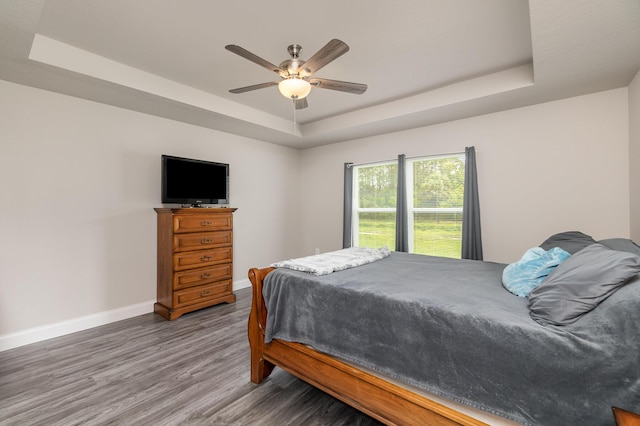 bedroom with hardwood / wood-style flooring, a raised ceiling, and ceiling fan