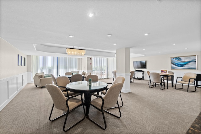 carpeted dining space featuring ornate columns and an inviting chandelier