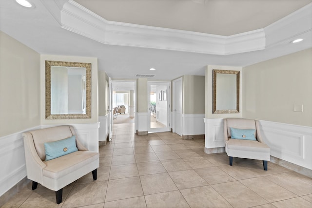 living area with a wainscoted wall, visible vents, a raised ceiling, and ornamental molding