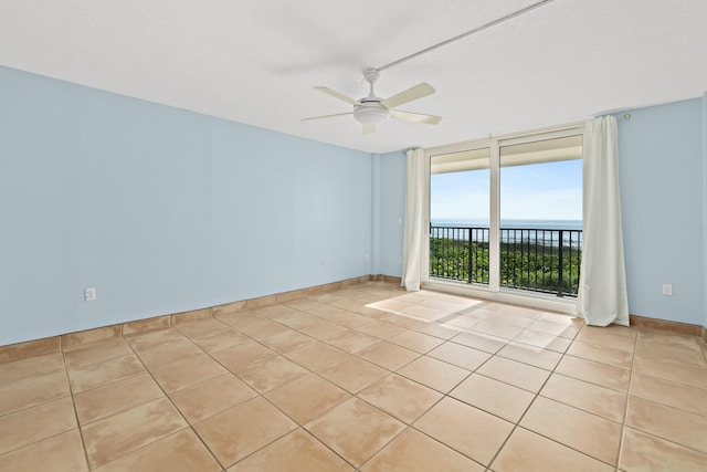 empty room with light tile patterned floors, a water view, and ceiling fan