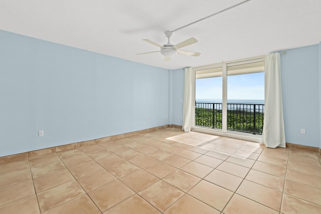 empty room with light tile patterned floors, a water view, a ceiling fan, and baseboards