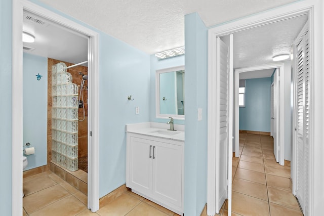 bathroom featuring a textured ceiling, vanity, visible vents, tiled shower, and tile patterned floors