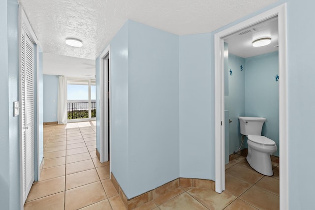 corridor featuring baseboards, visible vents, a textured ceiling, and light tile patterned flooring