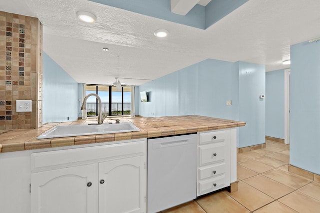 kitchen featuring tile countertops, white dishwasher, sink, a textured ceiling, and white cabinetry