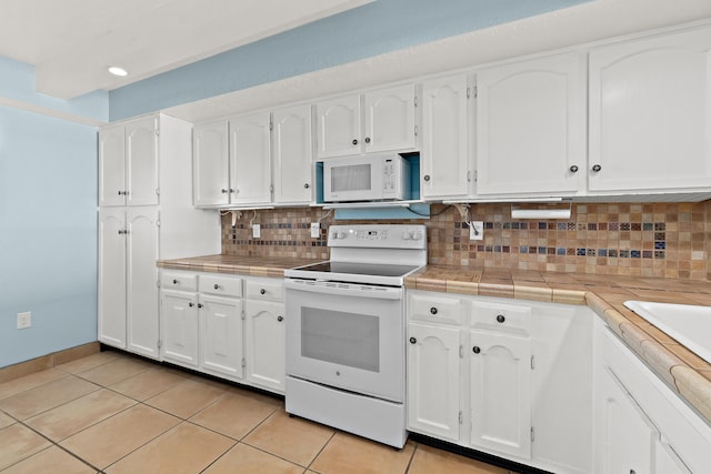 kitchen with tasteful backsplash, white cabinetry, light tile patterned flooring, and white appliances