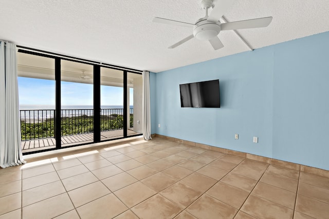 empty room with floor to ceiling windows, ceiling fan, a textured ceiling, a water view, and light tile patterned floors