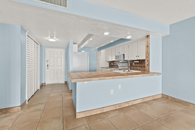 kitchen with white appliances, a textured ceiling, tile counters, white cabinetry, and kitchen peninsula