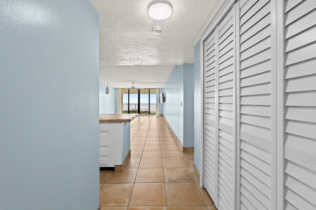 corridor featuring light tile patterned flooring, a textured ceiling, and baseboards