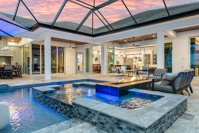 pool at dusk featuring ceiling fan, an in ground hot tub, glass enclosure, a patio area, and an outdoor hangout area