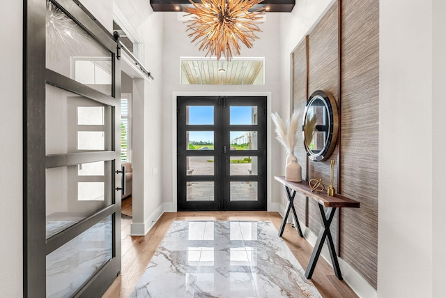 foyer entrance with a towering ceiling, a barn door, a chandelier, and light wood-type flooring